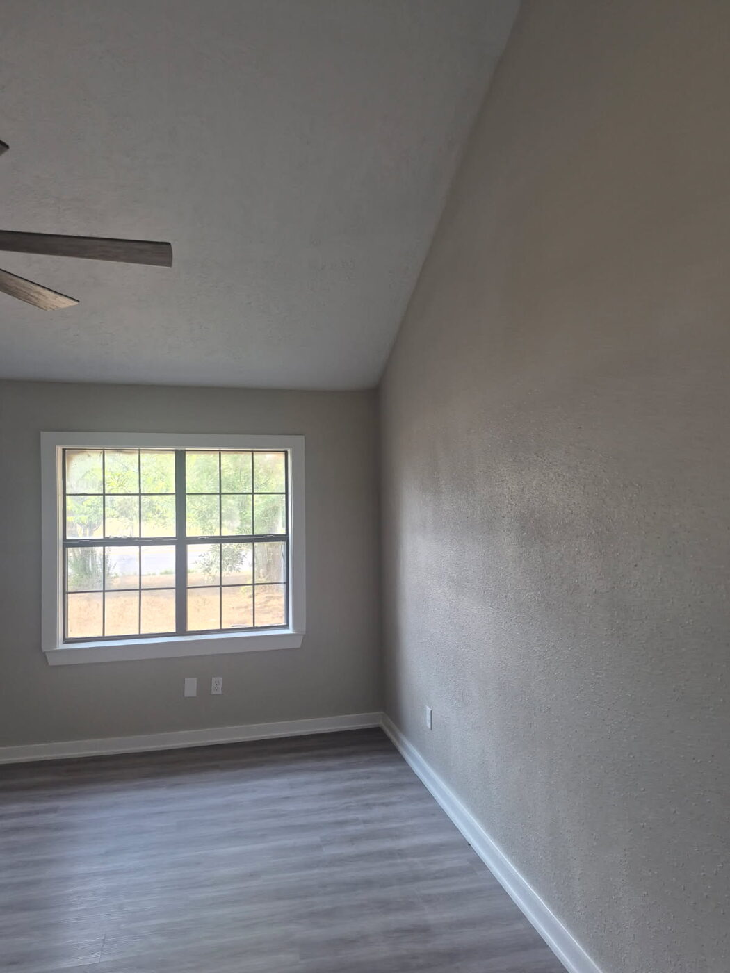 Bedroom with new gray plank flooring, white baseboards and a window