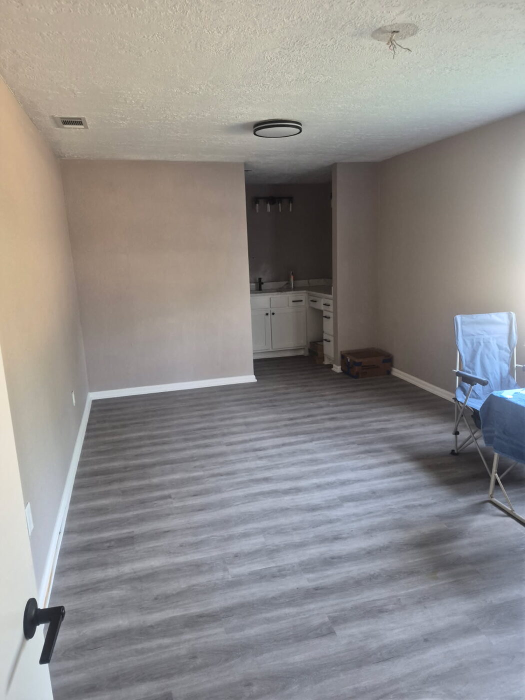 Room with new gray plank flooring opening to a kitchen area